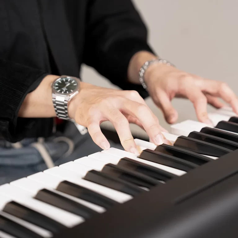 Close-up of hands playing a piano keyboard, wearing a silver wristwatch on the left wrist and a bracelet on the right wrist. ขายราคาพิเศษ