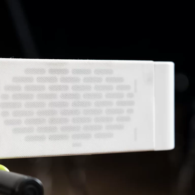 Close-up of a white perforated speaker grille against a dark background. ขายราคาพิเศษ