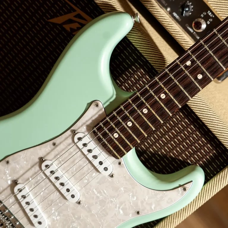 Mint green electric guitar with a white pickguard, shown close-up of body and fretboard on a textured amplifier backdrop. ขายราคาพิเศษ