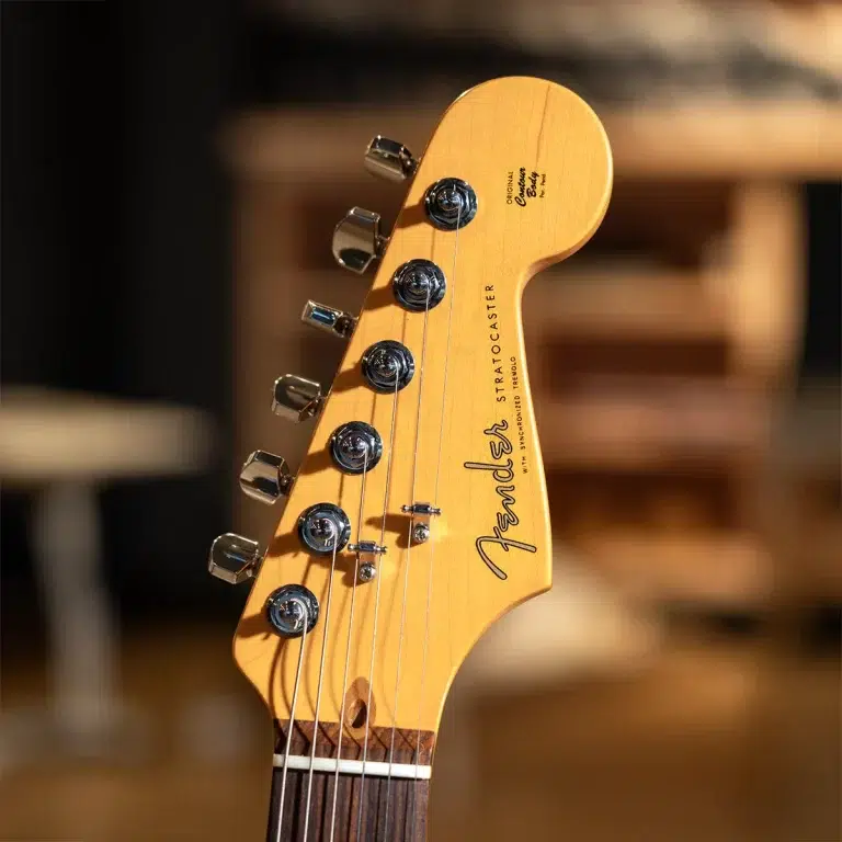 Close-up of a Fender Stratocaster headstock with tuning pegs, strings, and logo visible in warm wood tones. ขายราคาพิเศษ