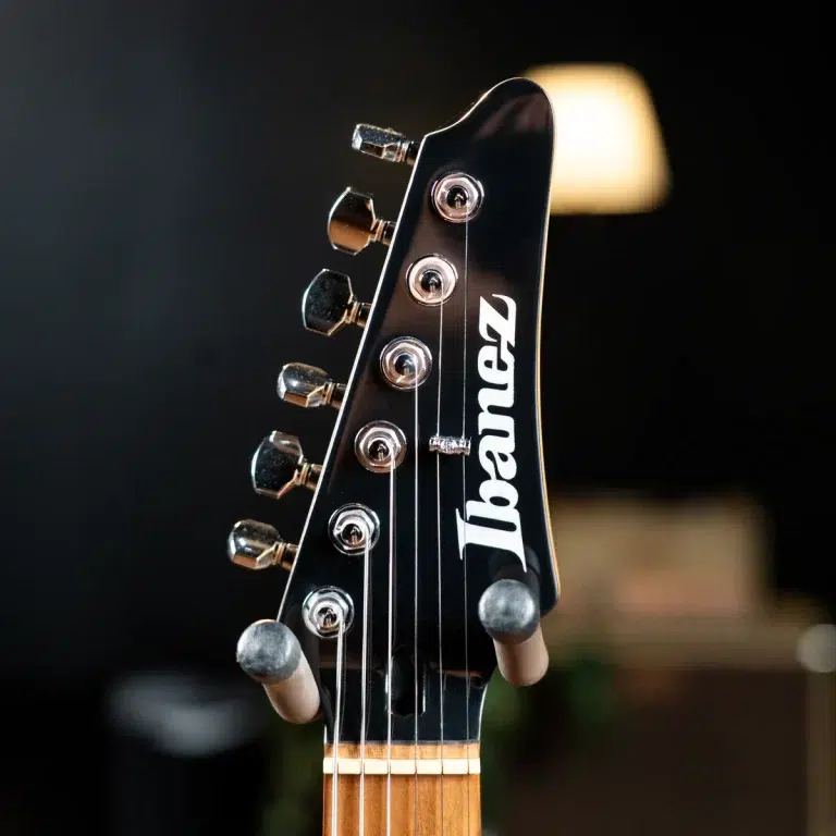 Close-up of an Ibanez guitar headstock with tuning pegs and strings, blurred background. ขายราคาพิเศษ