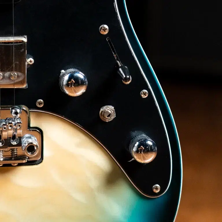 Close-up of a teal-edged electric guitar body showing chrome knobs, bridge, and pickguard hardware in sunburst finish. ขายราคาพิเศษ