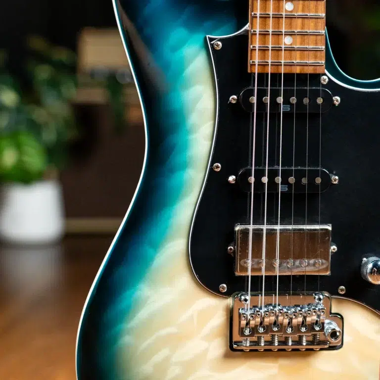 Close-up of an electric guitar body with a teal-to-cream gradient, black pickguard, two pickups, and a chrome bridge with strings visible. ขายราคาพิเศษ