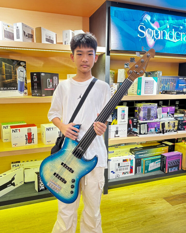 Boy in a white shirt holding a blue sunburst bass guitar in a music store.