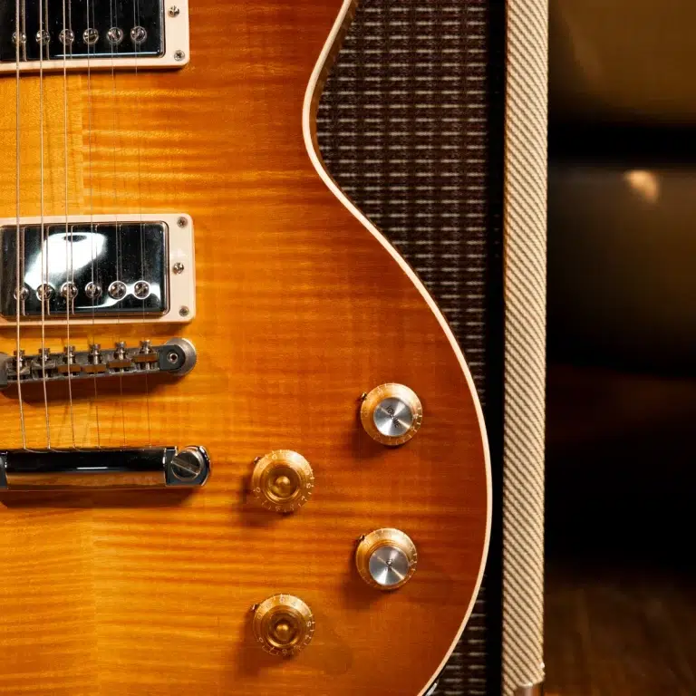 Close-up of an orange sunburst electric guitar showing pickups, strings, and control knobs with an amplifier grille in the background. ขายราคาพิเศษ