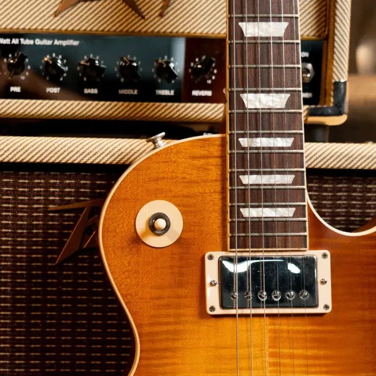 Sunburst electric guitar in close-up with chrome humbucker pickup and white pickup rings, set against a vintage amplifier backdrop ขายราคาพิเศษ