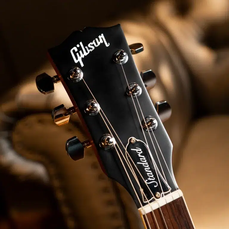 Close-up of a Gibson guitar headstock with six chrome tuners and strings, showing the 'Standard' inlaid badge and logo. ขายราคาพิเศษ