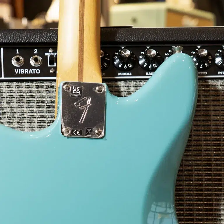 Teal electric guitar body with neck attached, resting against a vintage black amplifier with knobs visible. ขายราคาพิเศษ