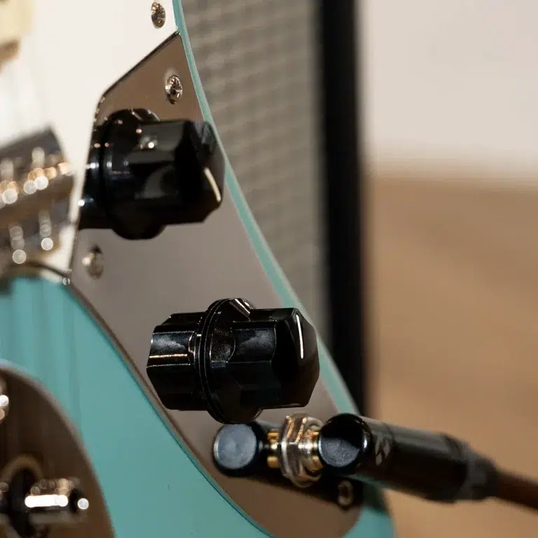 Close-up of a turquoise electric guitar body with an output jack and a plugged-in black cable, showing a control knob nearby. ขายราคาพิเศษ