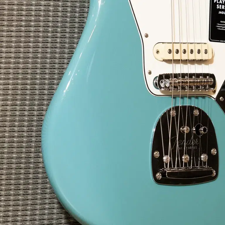 Turquoise Fender electric guitar body with a white pickguard and cream bridge, resting on a woven gray surface. ขายราคาพิเศษ