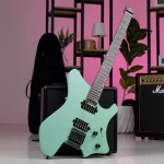 Mint-green electric guitar leaning on a black amplifier in a room with a pink wall, shelves, and a plant in the background. ขายราคาพิเศษ