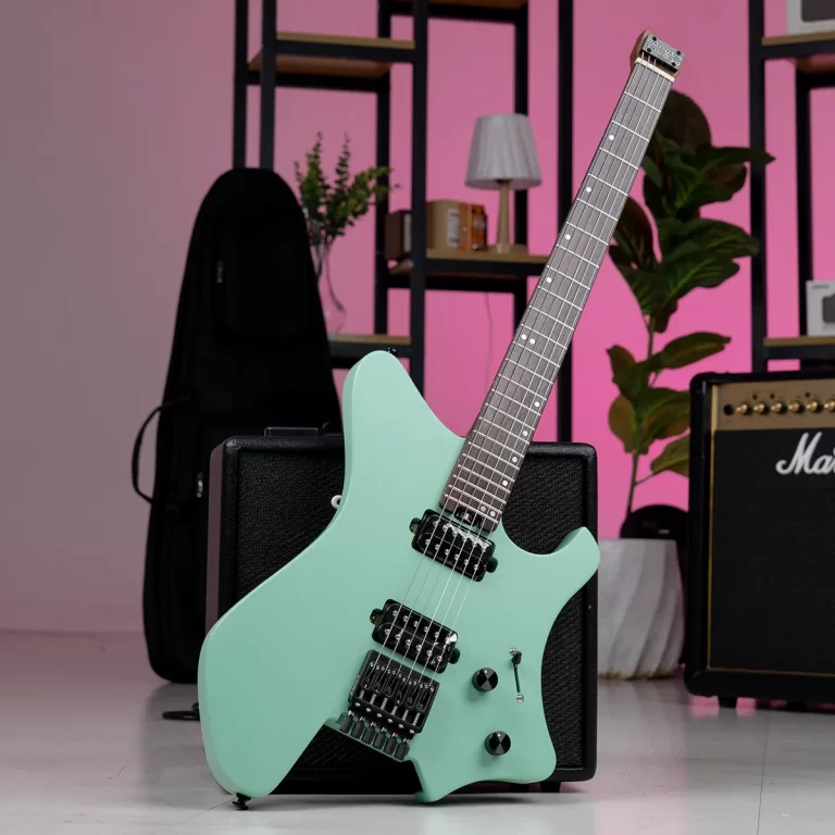 Mint-green electric guitar leaning on a black amplifier in a room with a pink wall, shelves, and a plant in the background. ขายราคาพิเศษ