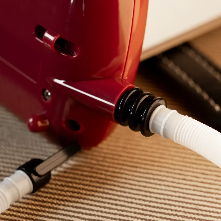 Close-up of a red vacuum cleaner hose connection with a black accordion seal and white hose, showing the intake area on the unit. ขายราคาพิเศษ