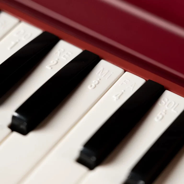 Close-up of a piano keyboard with white and black keys, captured at an angle beneath a red surface. ขายราคาพิเศษ