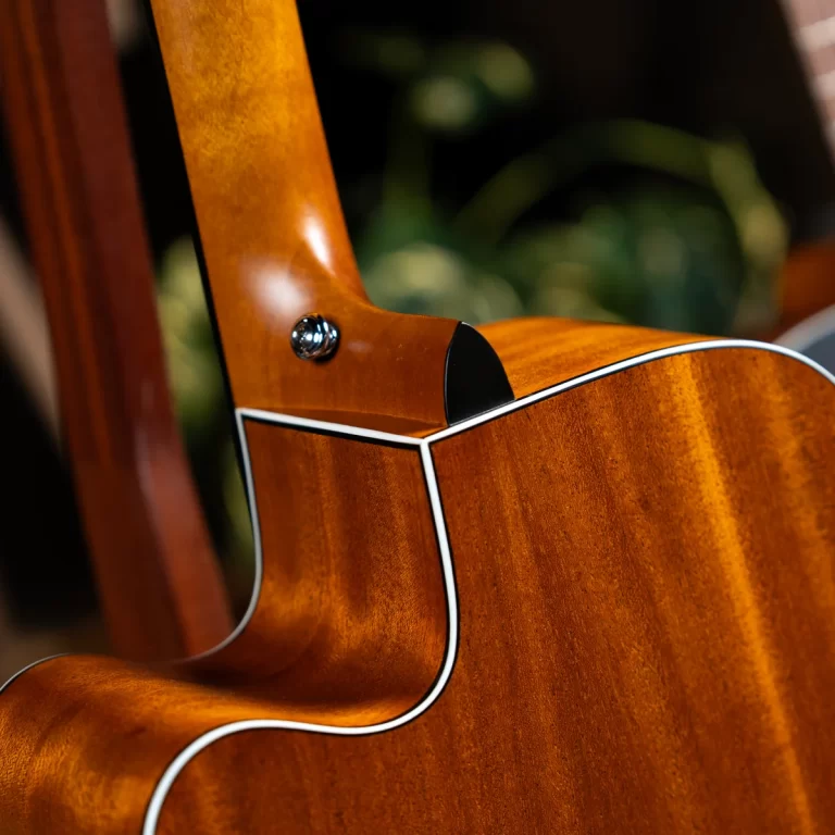 Close-up of a glossy wooden guitar with white binding, focusing on the neck joint and curve of the body. ขายราคาพิเศษ
