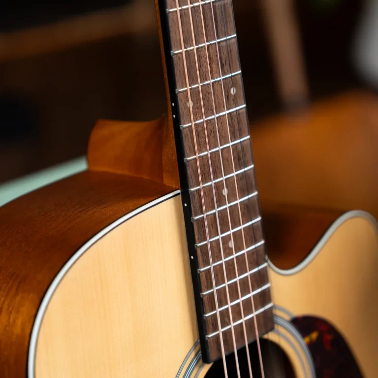 Close-up of an acoustic guitar neck and body, showing the fretboard, metal frets, and strings. ขายราคาพิเศษ