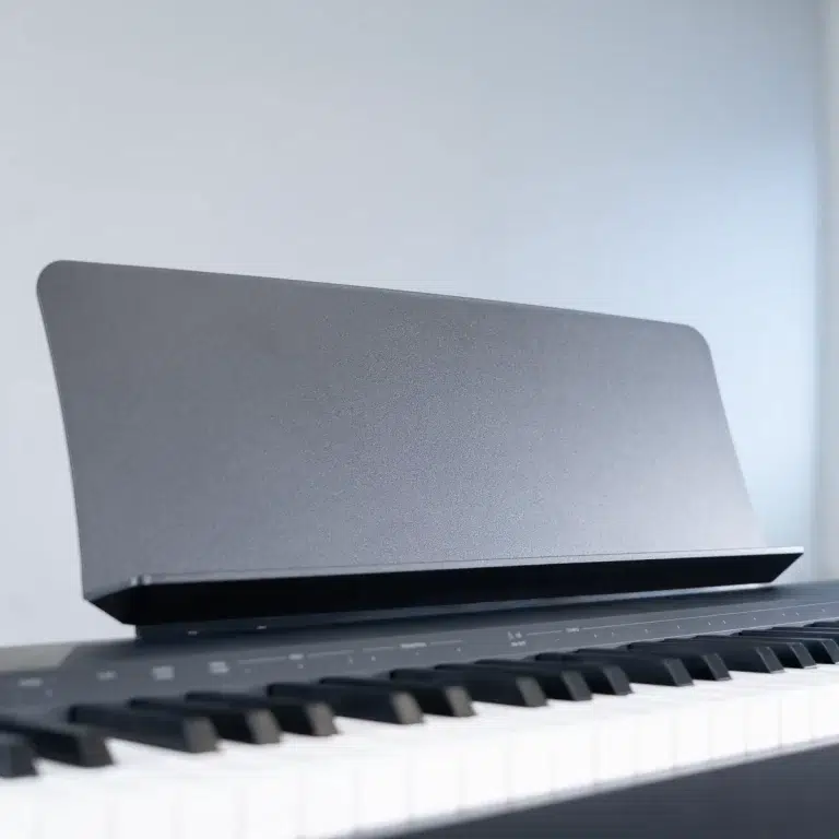 Close-up of a digital piano keyboard with a dark, angled music stand on the back edge. ขายราคาพิเศษ