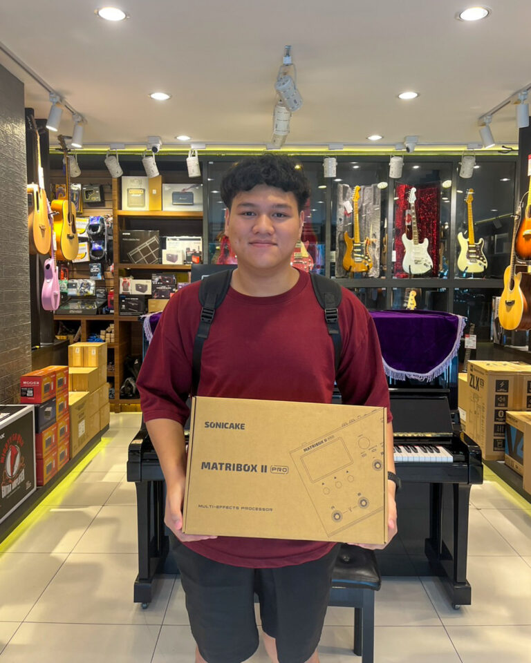 Young man in a music store holding a boxed SonicaKe Matribox II Pro multi-effects processor.
