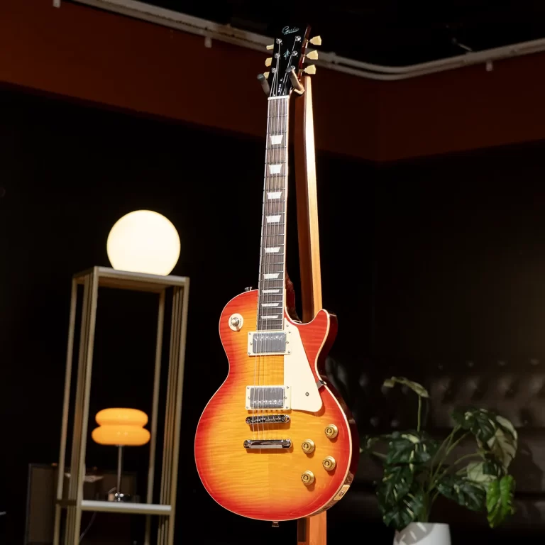 Sunburst electric guitar on a stand in a dim studio with a warm lamp in the background, and a plant nearby. ขายราคาพิเศษ