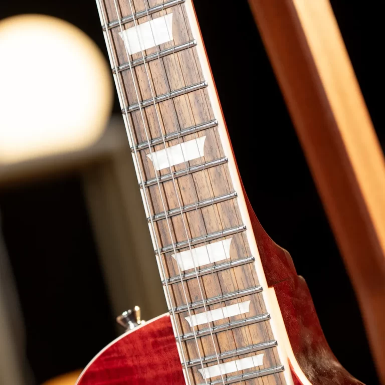 Close-up of a guitar neck showing frets, inlay markers, and strings on a wooden fretboard with a red body edge visible. ขายราคาพิเศษ