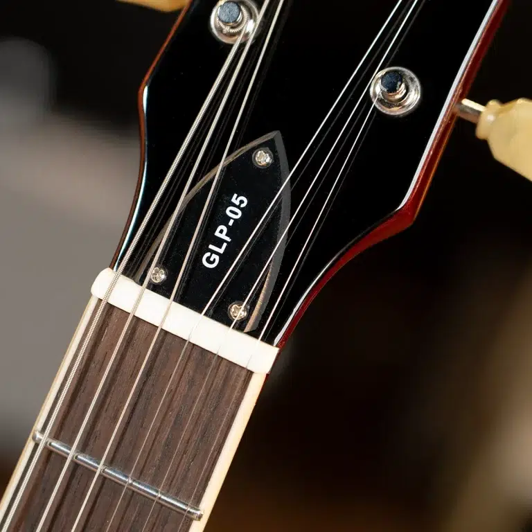 Close-up of a guitar headstock with tuning pegs and strings, showing a black plate reading GLP-05. ขายราคาพิเศษ