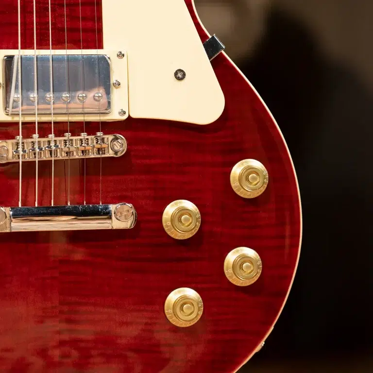 Close-up of a red electric guitar body showing gold knobs, strings, and chrome bridge with a cream pickguard piece nearby. ขายราคาพิเศษ