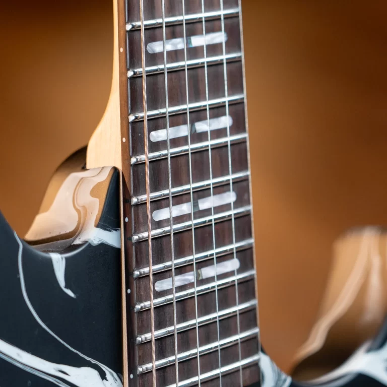 Close-up of an electric guitar neck showing frets, strings, and inlay markers on a dark fretboard. ขายราคาพิเศษ