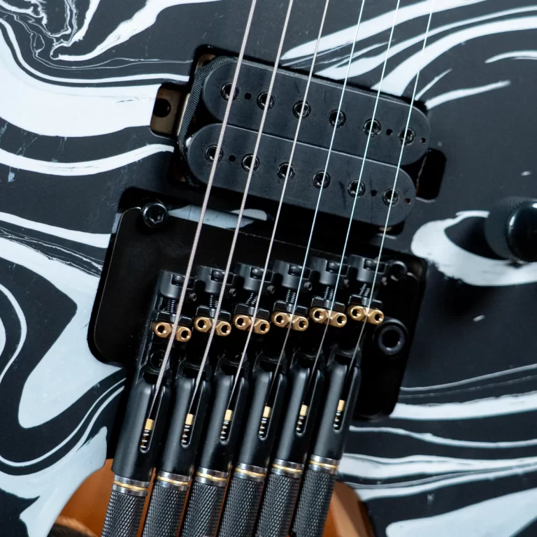Close-up of a black electric guitar bridge, pickups, and strings on a white-and-black marbled body pattern. ขายราคาพิเศษ