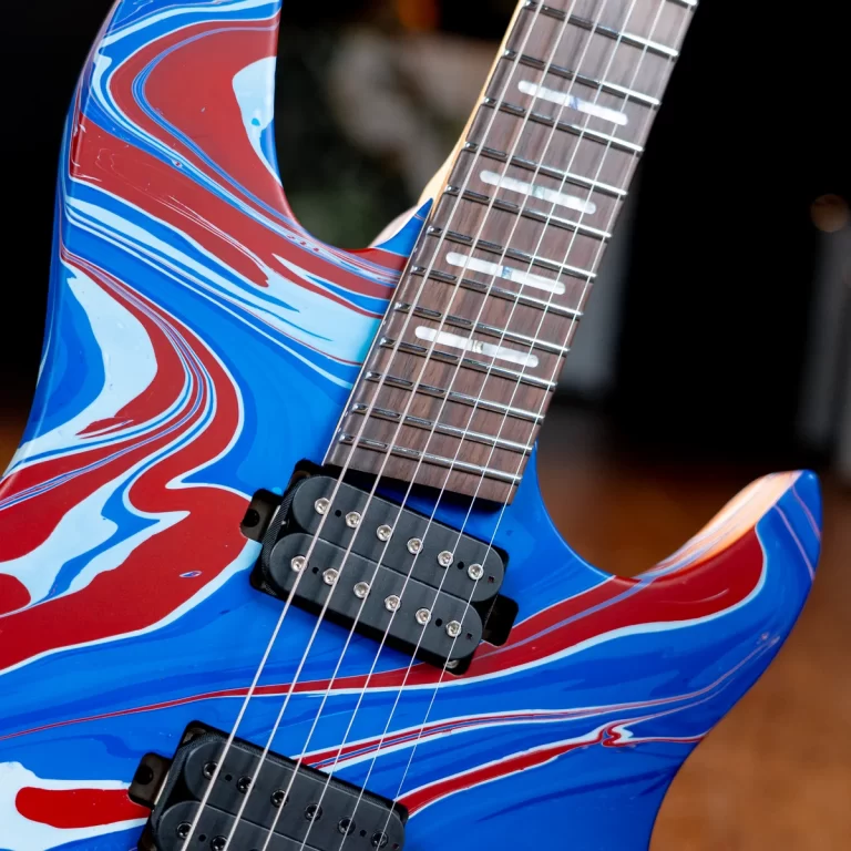Close-up of an electric guitar with a blue, red, and white swirled finish, showing the neck, frets, and pickups. ขายราคาพิเศษ