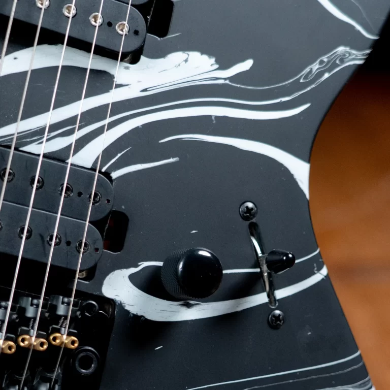 Close-up of a black electric guitar body with white paint streaks, showing strings, pickups, and control knobs. ขายราคาพิเศษ