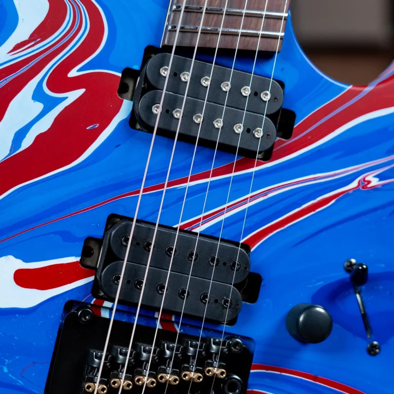 Close-up of a blue electric guitar with red and white swirls, showing two humbucker pickups and strings ขายราคาพิเศษ