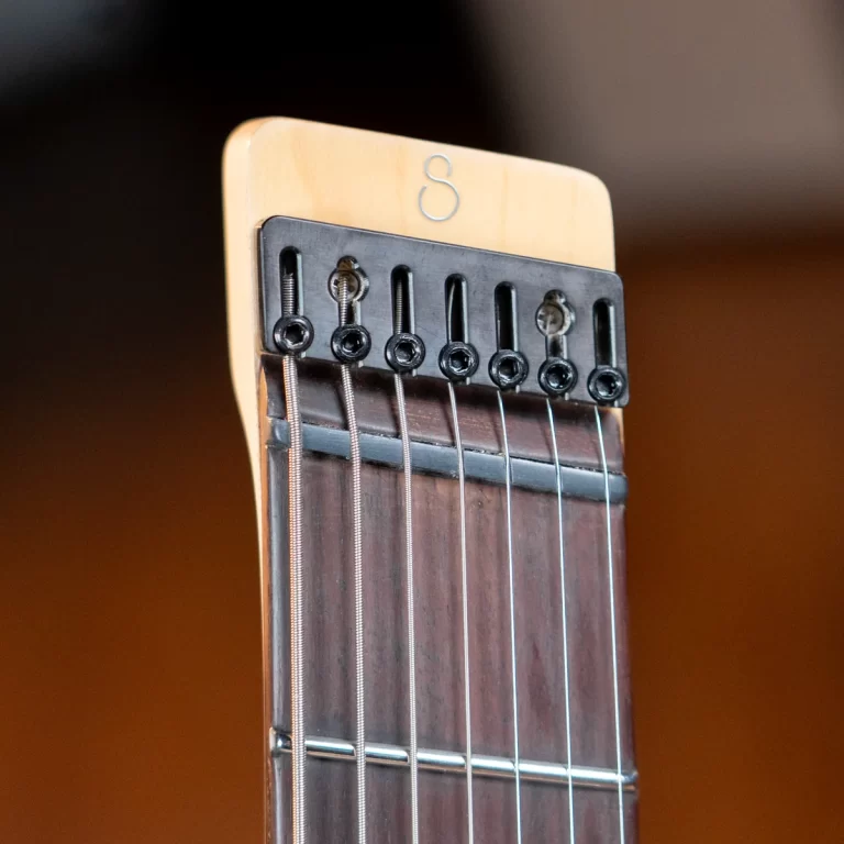 Close-up of a guitar headstock with six tuning pegs, strings, and nut visible against a warm background, showing steel strings and wood grain edge. ขายราคาพิเศษ
