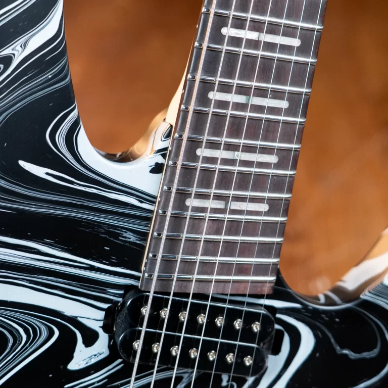 Close-up of a black marbled electric guitar body and fretboard with a humbucker pickup visible beneath the strings. ขายราคาพิเศษ
