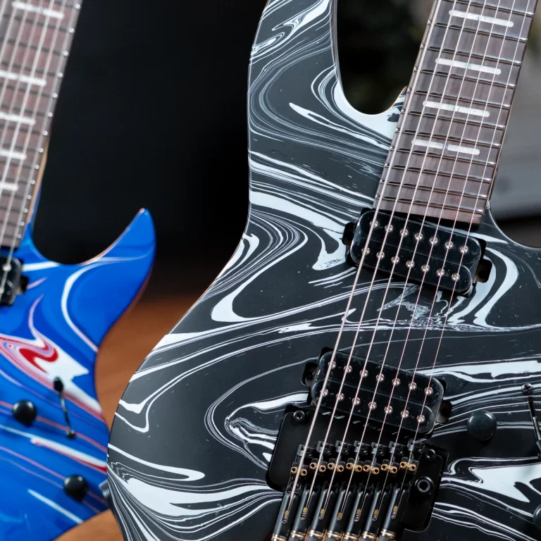 Close-up of a black-and-white marbled electric guitar with two humbucker pickups, partially flanked by a blue guitar on the left. ขายราคาพิเศษ