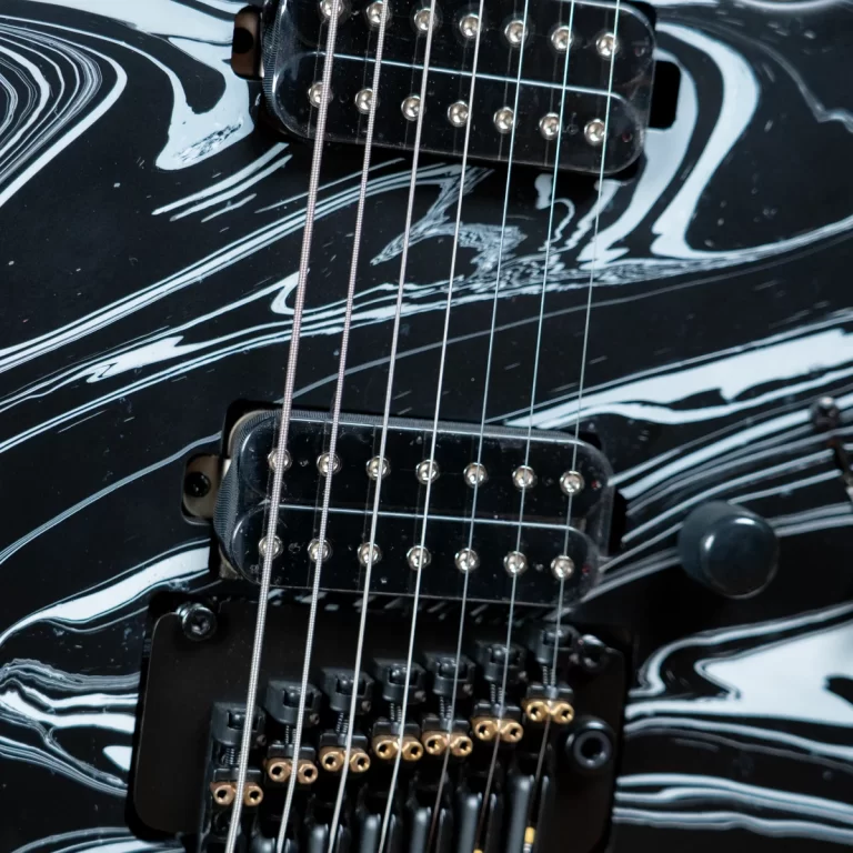 Close-up of an electric guitar showing two humbucker pickups and six metal strings over a black marbled body. ขายราคาพิเศษ