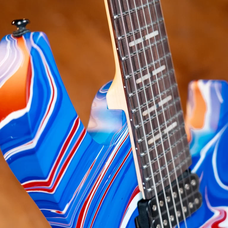 Close-up of a blue electric guitar body with red and white stripes and a dark fretboard edge visible in the foreground. ขายราคาพิเศษ