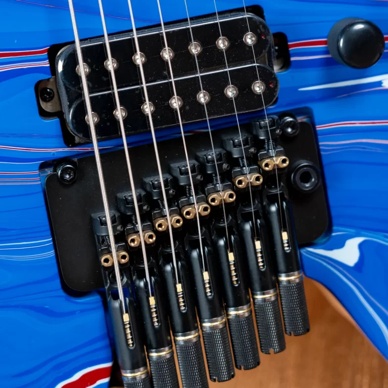 Close-up of a blue electric guitar bridge with six strings and metal saddles, showing the pickups and tremolo saddles nearby. ขายราคาพิเศษ