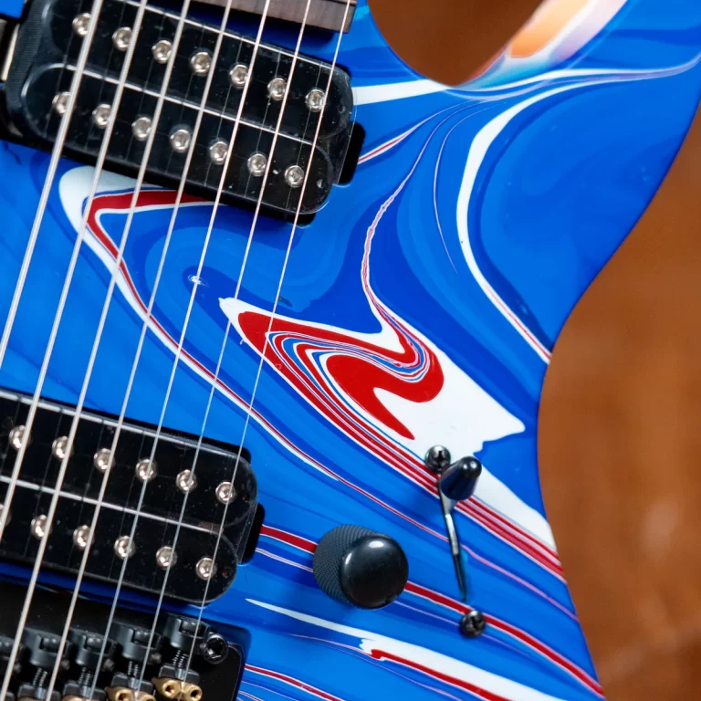 Close-up of a blue electric guitar body with two pickups, strings and control knobs visible, featuring a red/white swirl design. ขายราคาพิเศษ