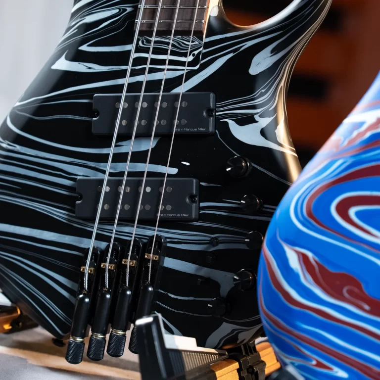 Close-up of a black electric guitar with a white marbled finish, two humbucker pickups, and metal strings; part of a blue and red swirled guitar is visible in the foreground. ขายราคาพิเศษ