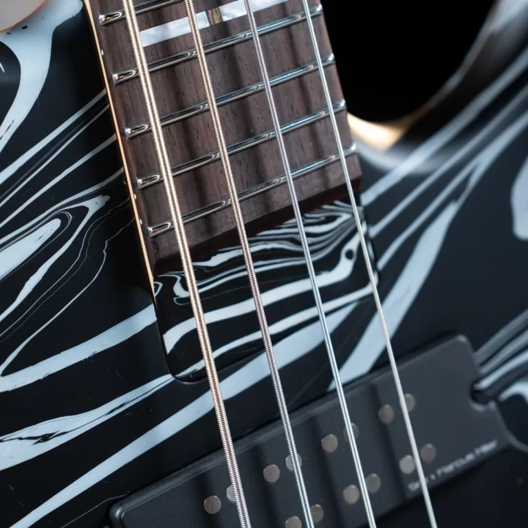 Close-up of an electric guitar neck and strings, showing chrome frets and six steel strings over a black marbled body. ขายราคาพิเศษ