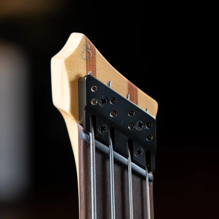 Close-up of a guitar headstock with tuning machines and steel strings against a dark background ขายราคาพิเศษ