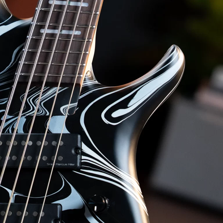 Close-up of a black electric guitar with white swirl designs, focusing on the strings and pickups on the body. ขายราคาพิเศษ