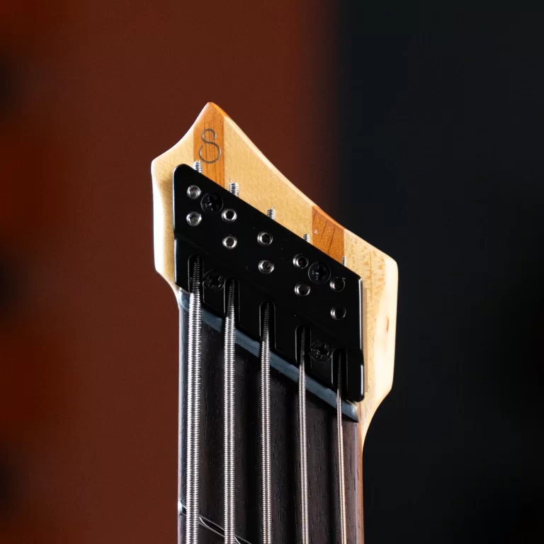 Close-up of a guitar headstock with six steel strings and tuners against a dark background, showing the wooden neck and hardware. ขายราคาพิเศษ