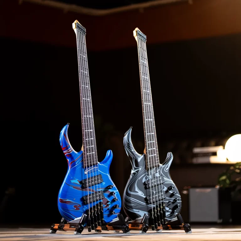 Two electric bass guitars with blue and gray marble finishes, standing on floor stands on a dark stage porch light behind them. ขายราคาพิเศษ