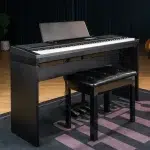 Black digital piano with a padded bench on a wooden stage floor in a studio setting with a dark curtain backdrop ลดราคาพิเศษ