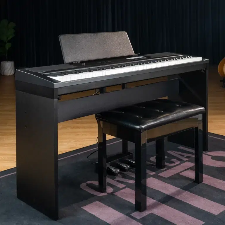 Black digital piano with a padded bench on a wooden stage floor in a studio setting with a dark curtain backdrop ขายราคาพิเศษ