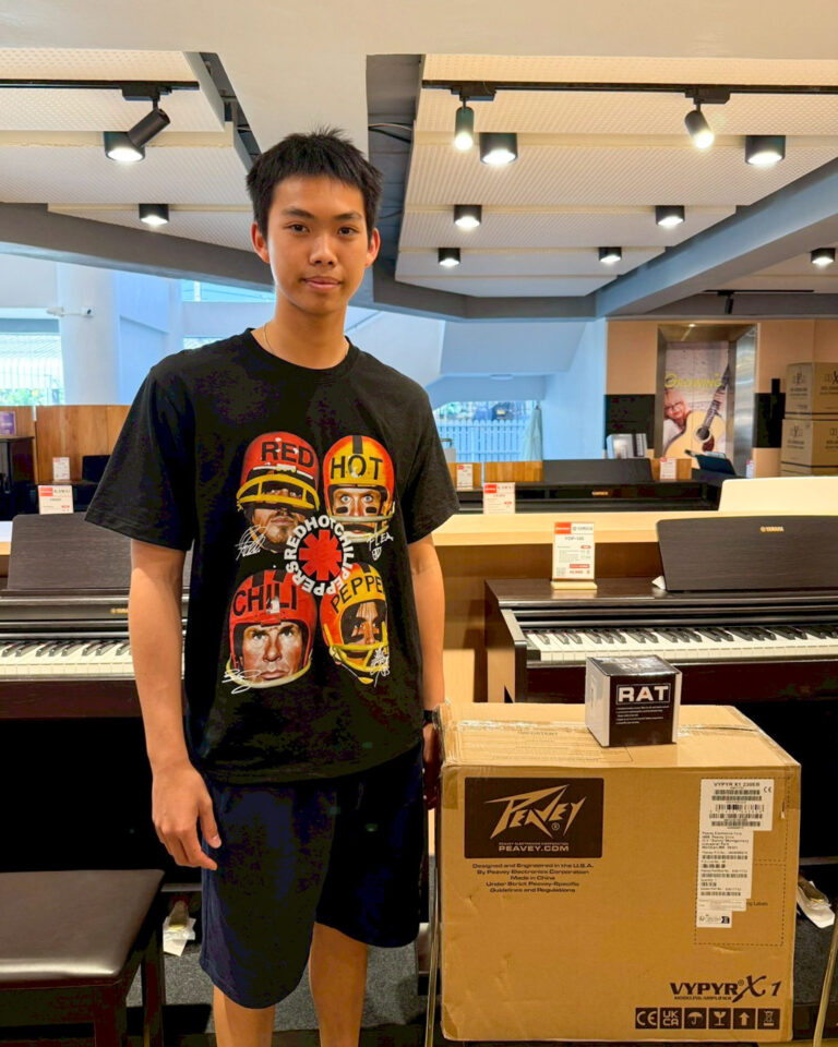 Teenager in a black graphic T-shirt stands beside electronic pianos in a music store.