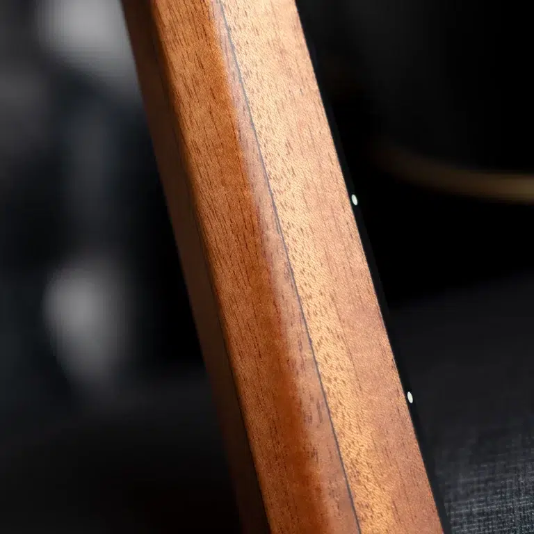 Close-up of a warm wooden guitar neck showing grain and a dark edge against a black background. ขายราคาพิเศษ