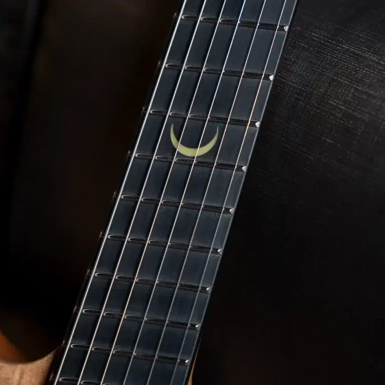 Close-up of a guitar neck fretboard showing a pale crescent moon inlay among the metal frets and strings ขายราคาพิเศษ