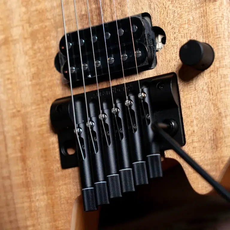 Close-up of an electric guitar bridge and pickup on a natural wood body, with six steel strings over black saddles. ขายราคาพิเศษ